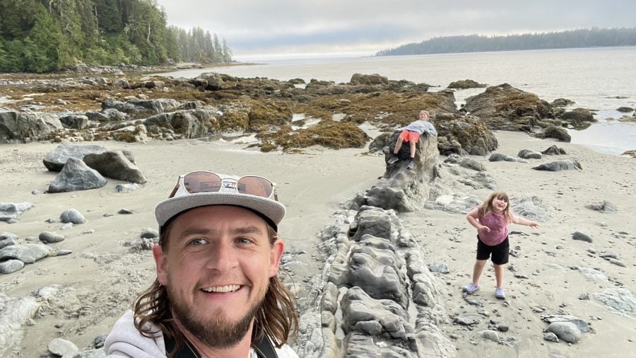 Walt and his kids are sitting on rocks in the sand.