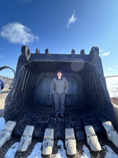 Lucas Maxon stands inside the large bucket of a surface mining haul truck, illustrating the massive scale of the equipment.