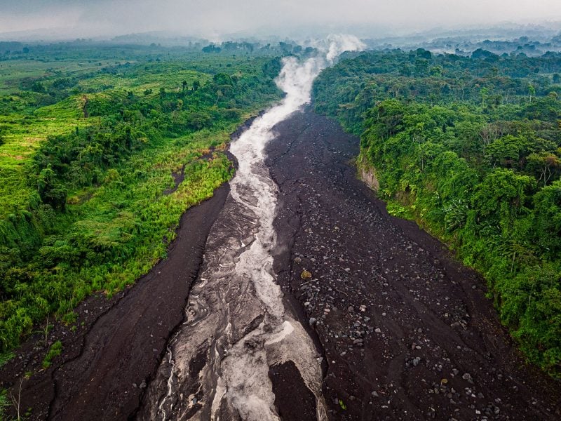 Aerial view of a lahar moving down a volcano, showing a muddy, debris-filled flow cutting through the landscape.