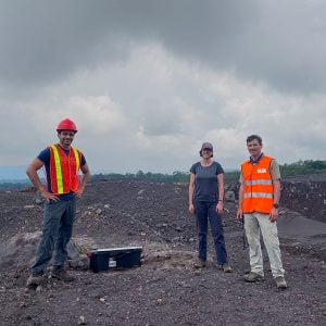 Dr. Gustavo Bejar-Lopez, Dr. Alexander Bartel, and Dr. Gregory Waite stand together on the summit of a volcano with rocky terrain and clouds in the background.