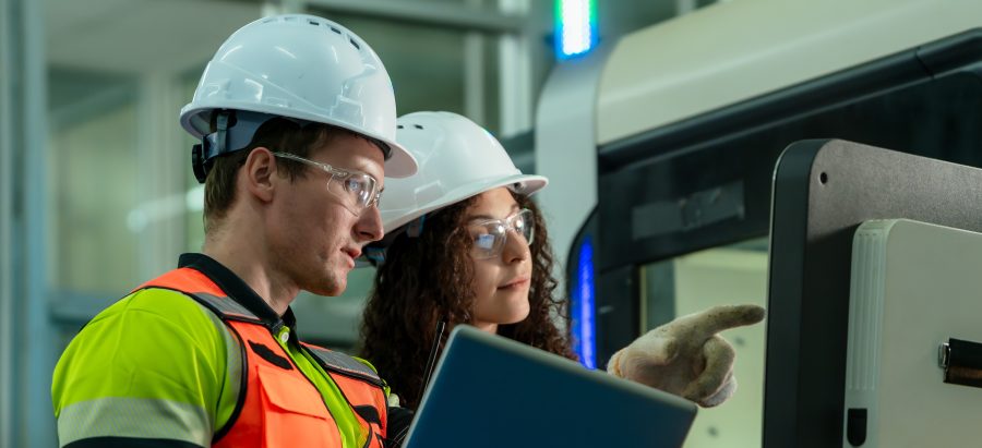 Two engineers in a factory look at a monitor.