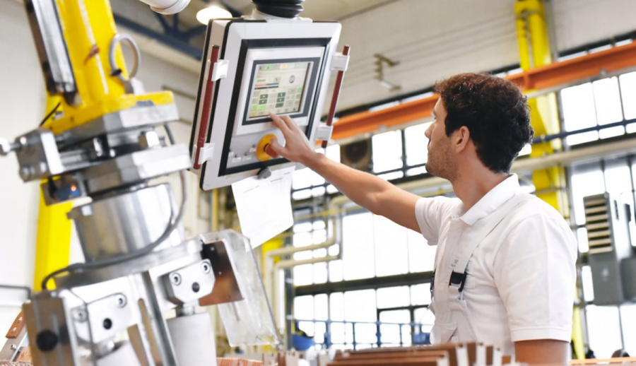 A young manufacturing engineering professional touches a computer monitor while in a factory setting.