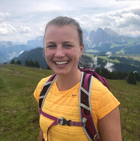 Anne Mortvedt wearing a backpack standing on a hillside with mountains and clouds behind