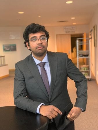 Revanth Mattey leaning against a table, indoors, wearing suit and tie