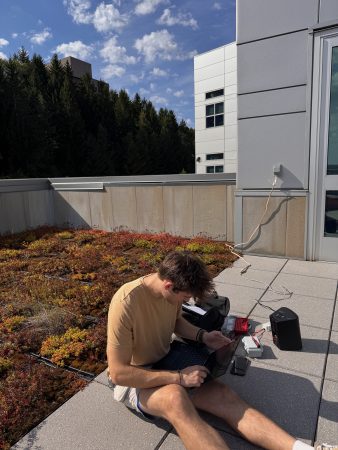 a student works on his laptop next to a project he is setting up near the green roof at the GLRC