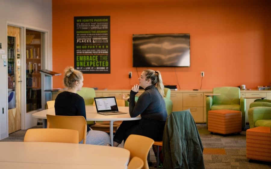 Two students sitting at a table working on a laptop in the Pavlis Honors COllege space