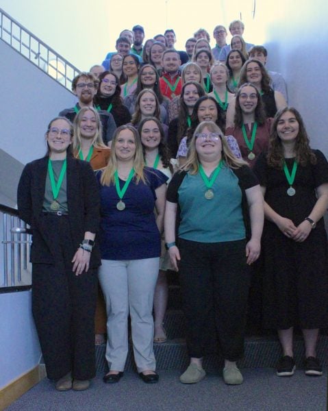 students standing in rows wearing medals with green ribbons
