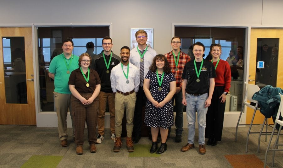 9 of the 10 pavlis honors college student graduates posing with smiles and wearing their medallion around their neck with a green ribbon