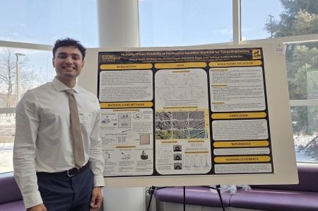 student standing next to their undergraduate research poster