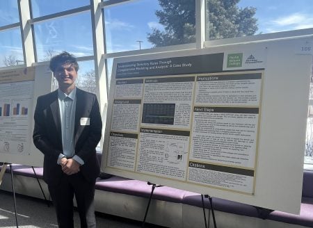 student standing next to their undergraduate research poster