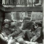 Black and white photo of three children sleeping on the street.