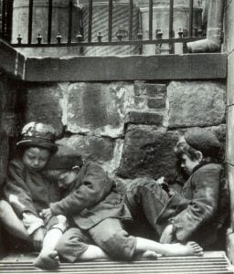 Black and white photo of three children sleeping on the street.