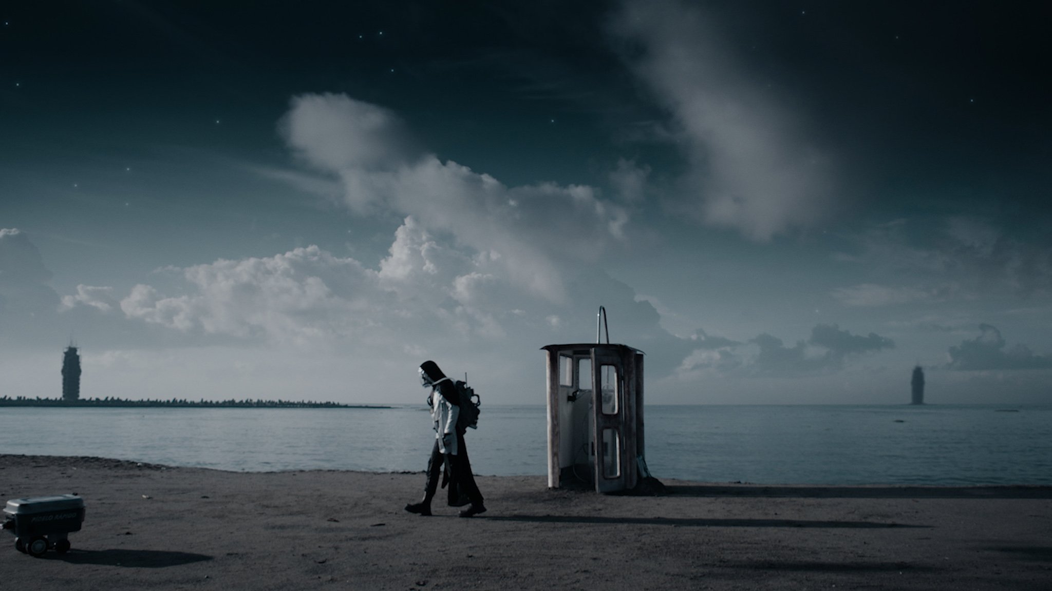 Still from the film showing a gray, dystopian landscape with a small doorway to an elevator shaft in the middle of the frame. A figure in a full-face oxygen mask walks to the left.