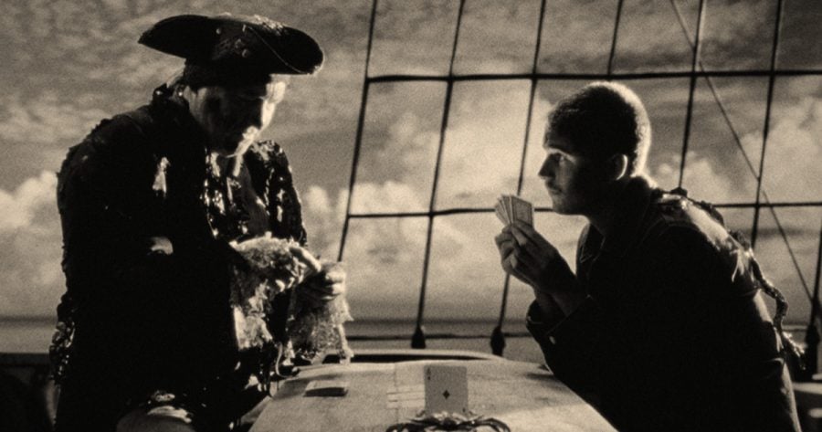 The Peril at Pincer Point. Two men in period costume play cards aboard a ship in a black-and-white film scene.