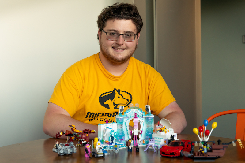 A young man wearing a Michigan Tech t-shirt sits with LEGO products at a table.