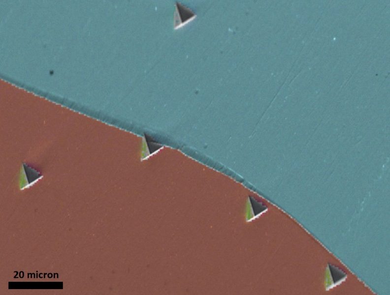 Microimage of iron shows triangular indentations, like small pyramids, at the brown/green grain boundary.