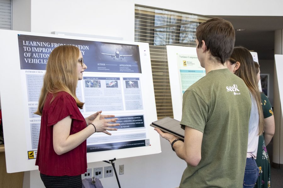 Presenter standing by her poster, with attendees in the background.