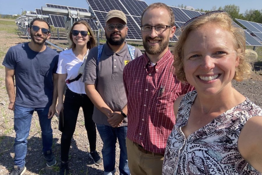 Group of five people standing outside near a solar panel array.