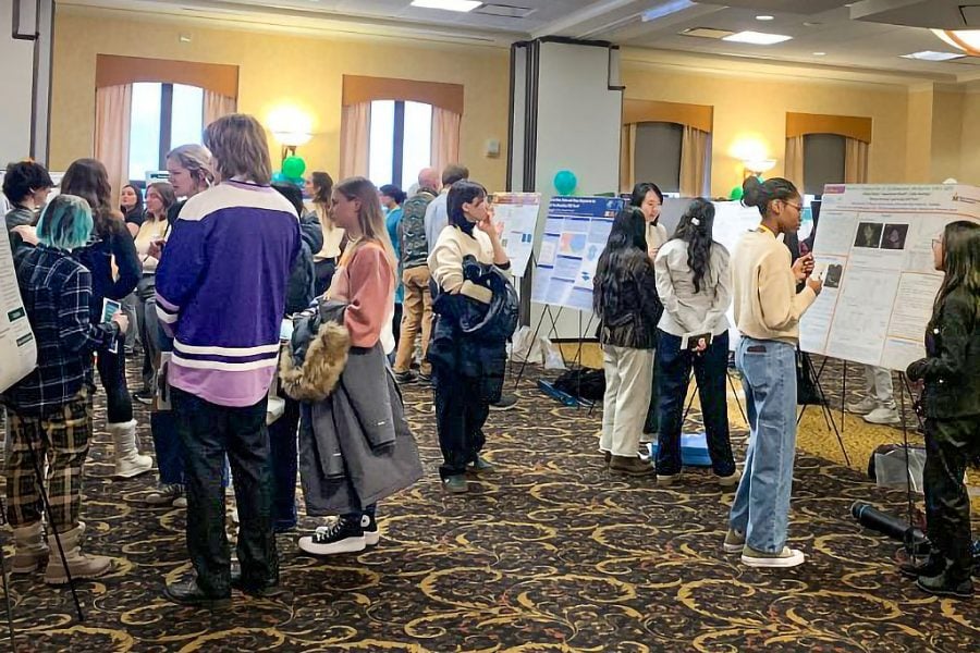 Conference attendees gather in front of informational posters in the Memorial Union Building Ball Room. One visible poster facing the camera reads “CU*iP at Michigan Tech Futures Festival Materials & Medical Physics Posters.