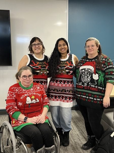 Four people standing in a group wearing festive holiday sweaters