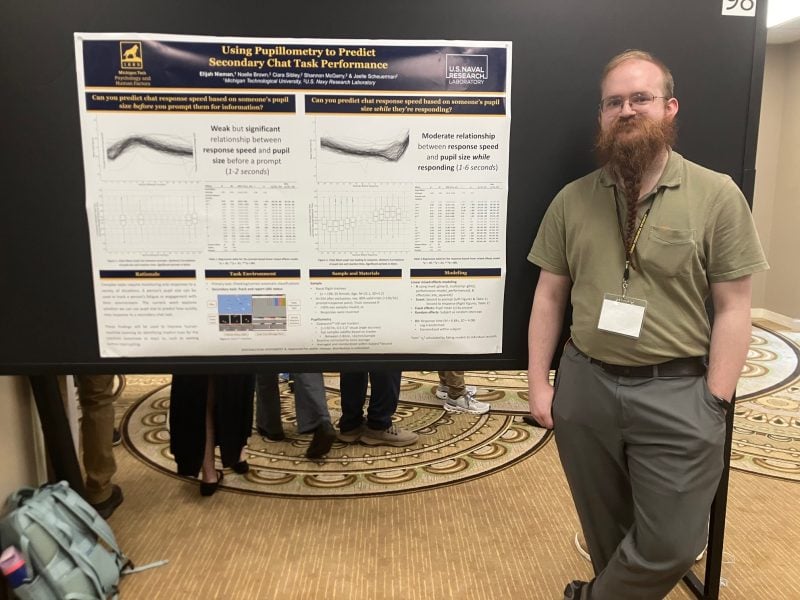 Elijah Nieman standing to the side of his research poster "Using Pupillometry to Predict Secondary Chat Task Performance" 