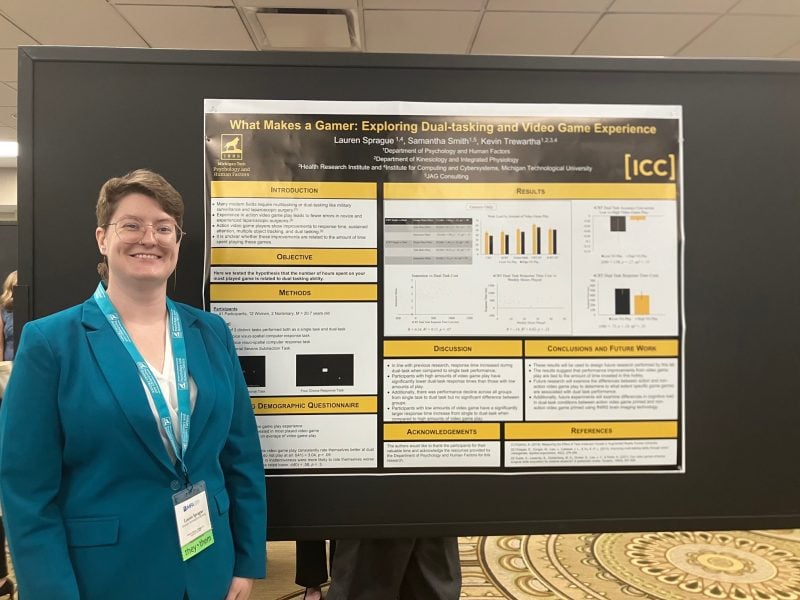 Lauren Sprague standing next to their research poster “What Makes a Gamer: Exploring Dual-Tasking and Video Game Experience.”