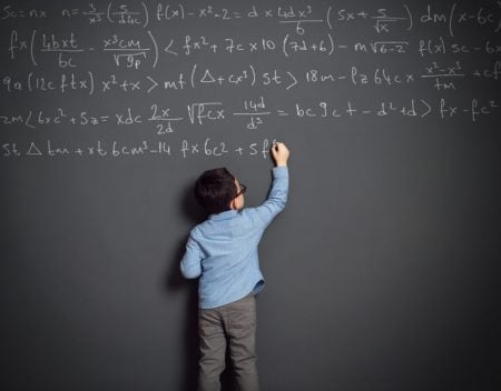 little boy standing in front of a large blackboard writing a long equation