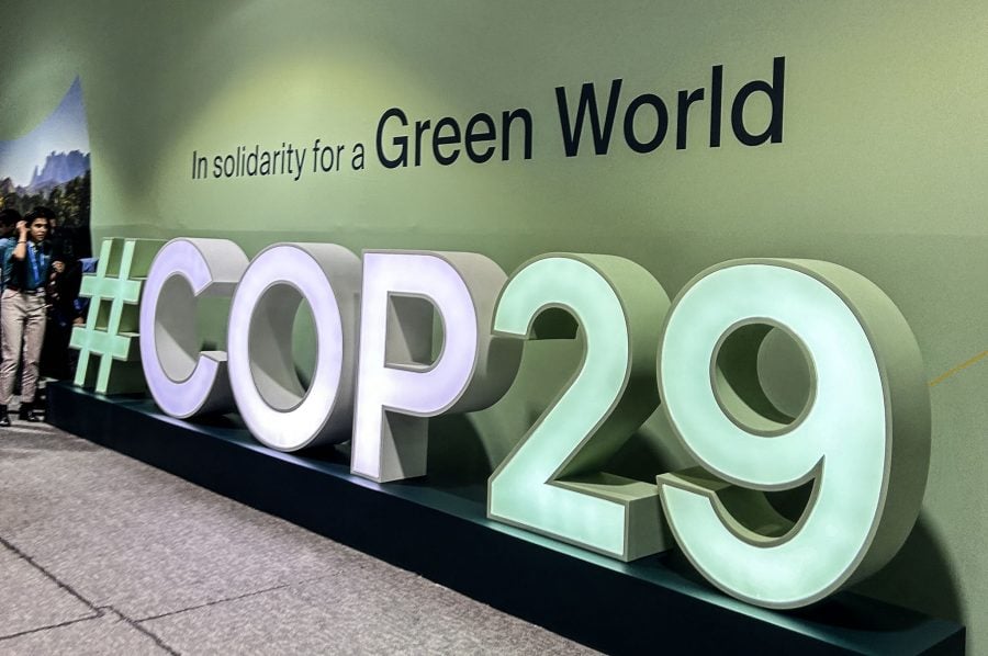 A large three-dimensional sign saying #COP29 stands in front of a green interior wall. The wall above the sign reads, “In solidarity for a Green World”.