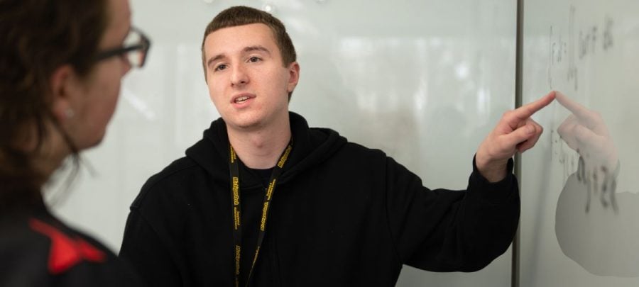 Discrete mathematics student McCoy Ziehl gestures to a math problem on a white board in the Math Learning Center while talking to another student.