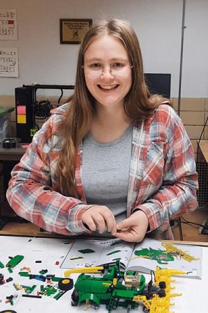 Emily Ruf sits smiling at a table, working on a John Deere Lego set.