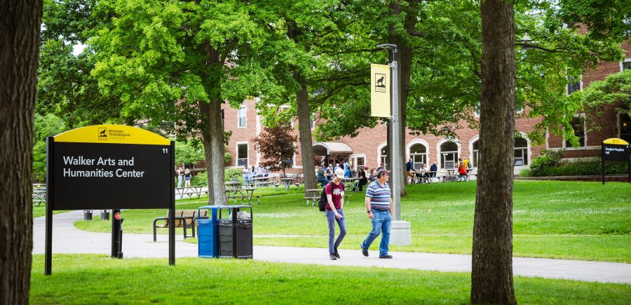 Students walking on campus by the Walker Arts and Humanities Center sign.