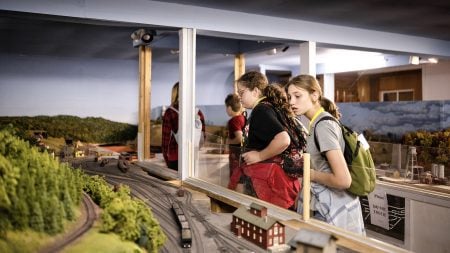 SYP students lean over a plexiglass barrier to view a model train track showing a historical scene from the Keweenaw Peninsula.