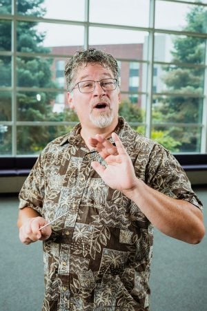 Joel Neves poses singing with his conductor’s baton in the Rosza lobby on Michigan Tech’s campus.