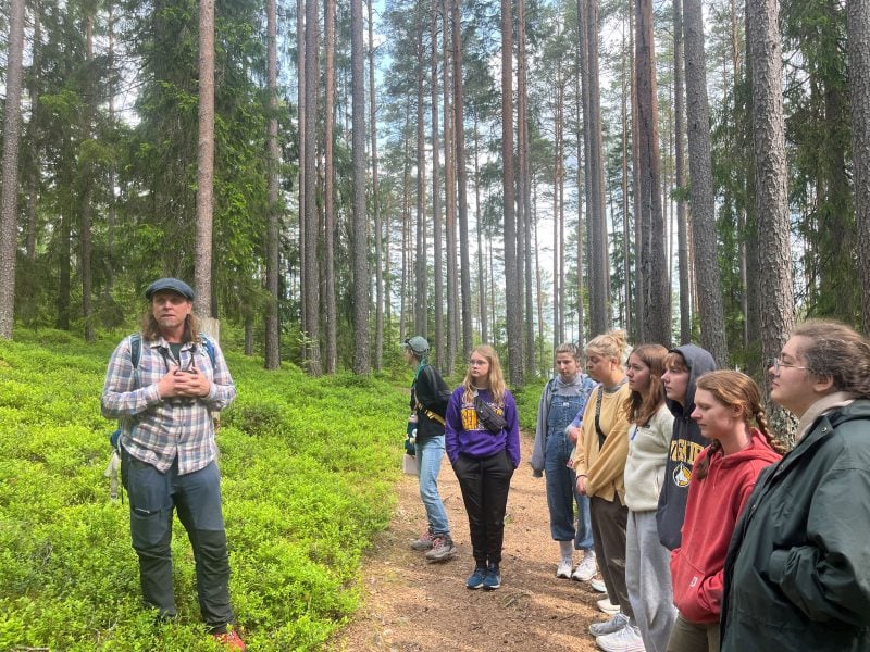 students standing on a forest trail with a ecologist standing on plants in a pine forest