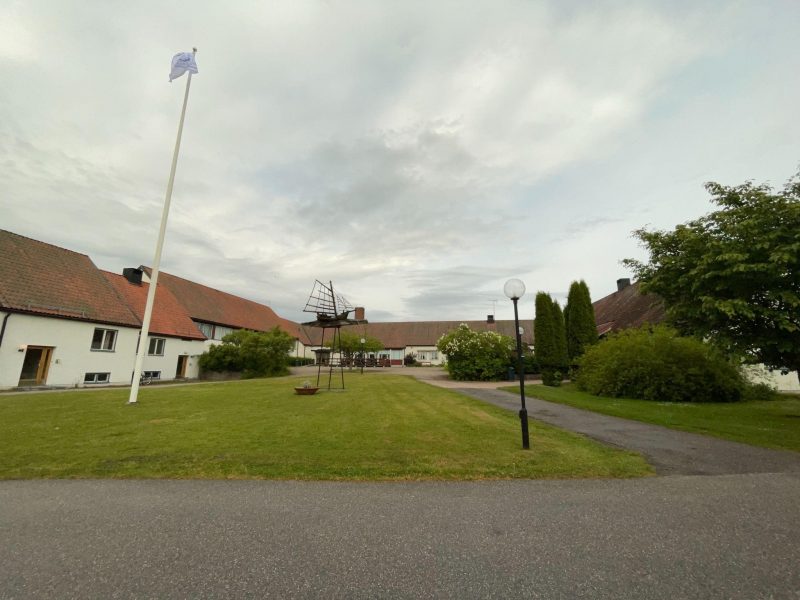 a view of a building with green space in front, a flagpole, streetlight, and a small statue of a ship