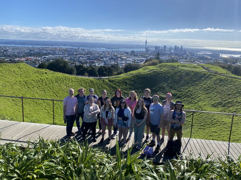 Students posing atop Maungawhau with downtown Auckland in the background.